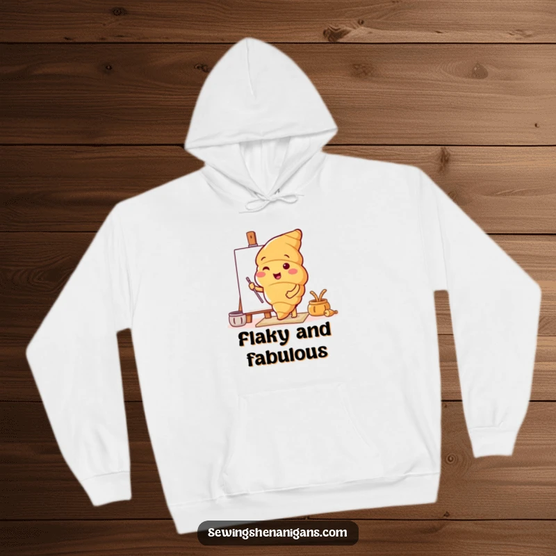 Funny hoodie displaying a happy croissant character joyfully testing a new, intricate pattern, offering warmth and style.
