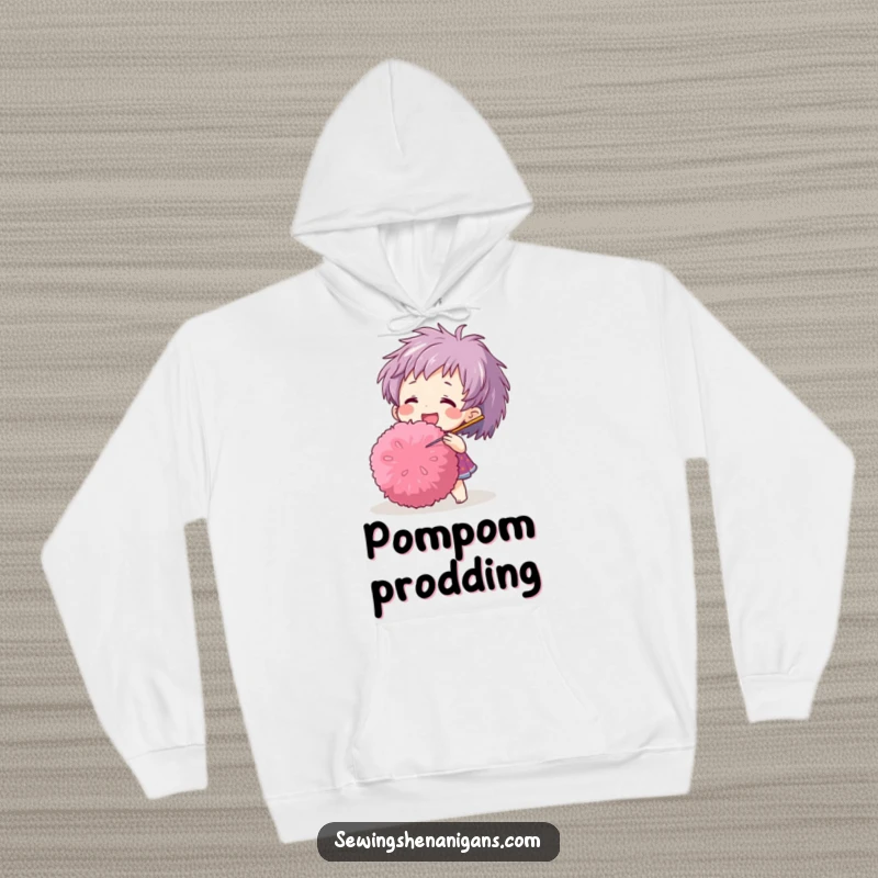 Funny hoodie with a happy character adorably poking a large pom-pom with a needle, designed for comfort and humor.